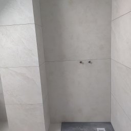 Rafkam - Wykończona kabina prysznicowa z jasnymi płytkami i odpływem liniowym w Kartuzach. Widoczne przyłącza wodne i pion z obudową z płytek.