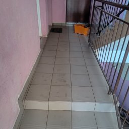 Rafkam - Wyłożone płytkami schody na klatce schodowej z różową ścianą i metalową barierką. Widoczny kuweta z narzędziami. Świeżo położone płytki na schodach.