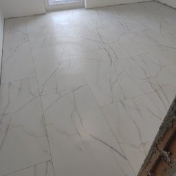 Rafkam - Wykończona podłoga z płytek imitujących marmur w jasnym pomieszczeniu z oknem. Fragment ściany z cegły w prawym dolnym rogu. Widok z góry, ukośnie.