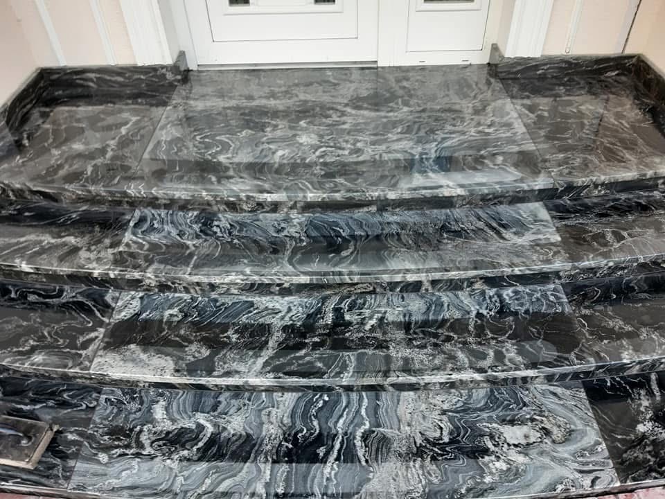 Wykończone marmurowe schody wejściowe z widocznym wzorem żyłkowania, prowadzące do białych drzwi wejściowych, z delikatnym oświetleniem.