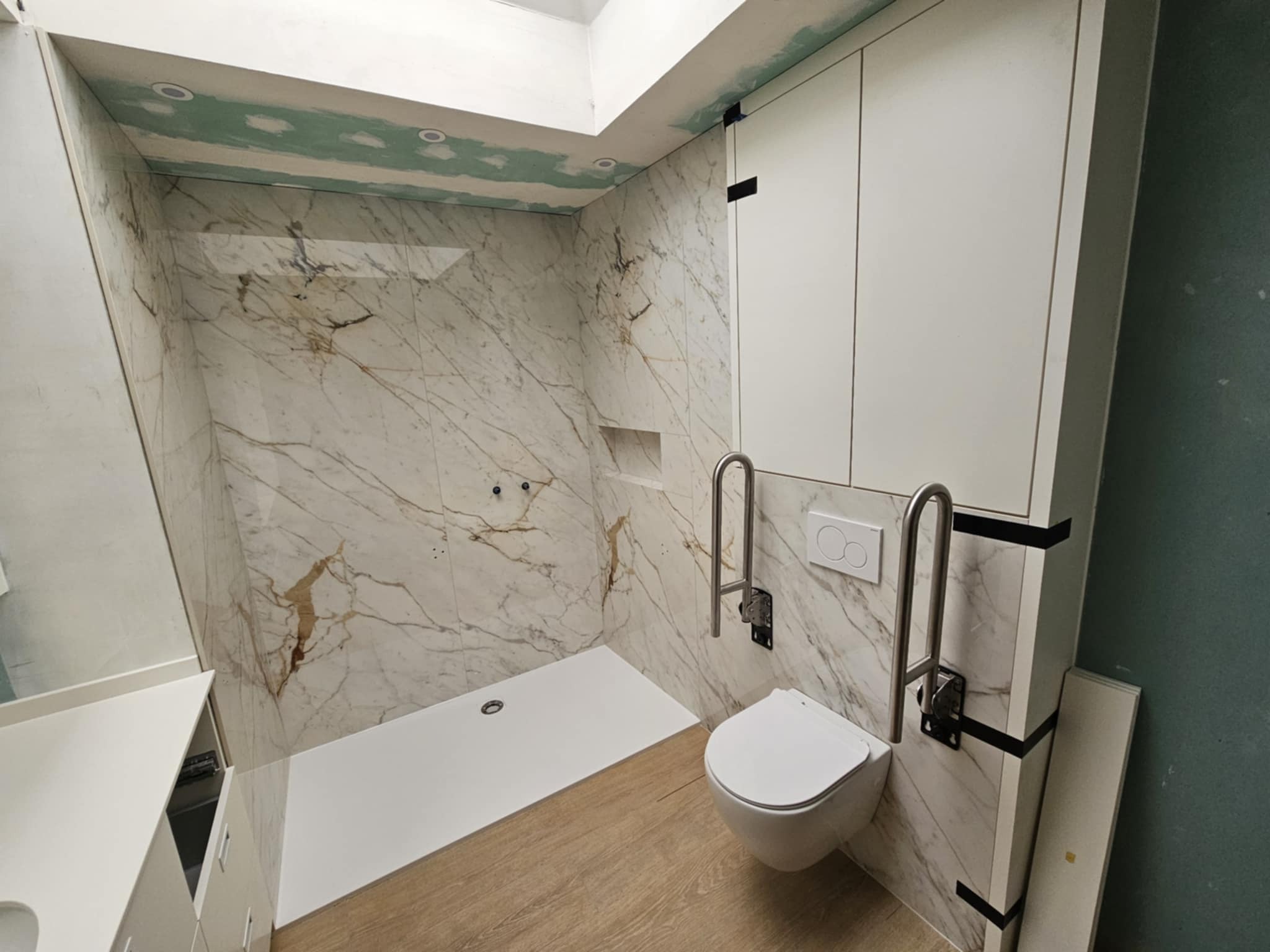 Wykończona łazienka z marmurowymi płytkami i kabiną prysznicową typu walk-in, widok z perspektywy. Realizacja w Kartuzach. Umywalka z szafką i toaleta.