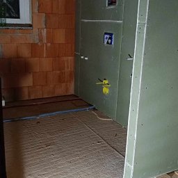 Oskar Czernecki - Wnętrze w trakcie remontu: ściana z cegły, płyty gipsowe, instalacja elektryczna i wodna, wylewka podłogowa. Widoczny wiertarko-wkrętak.