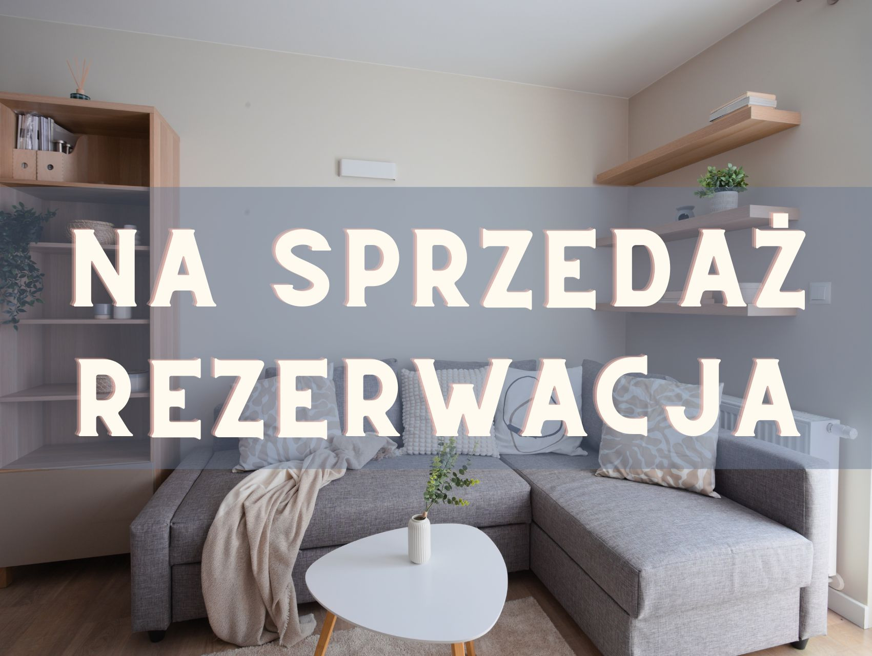 Jasne wnętrze salonu z szarą sofą narożną i białym stolikiem. Na zdjęciu widoczny napis 'Na sprzedaż Rezerwacja'.