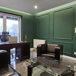 Kancelaria Adwokacka Adwokat Adam Mroczkowski - Eleganckie biuro z zielonymi ścianami, ciemnymi meblami, biurkiem z laptopem i figurką Temidy. Widok z okna na drzewa. Marmurowa podłoga i szklany stolik kawowy.
