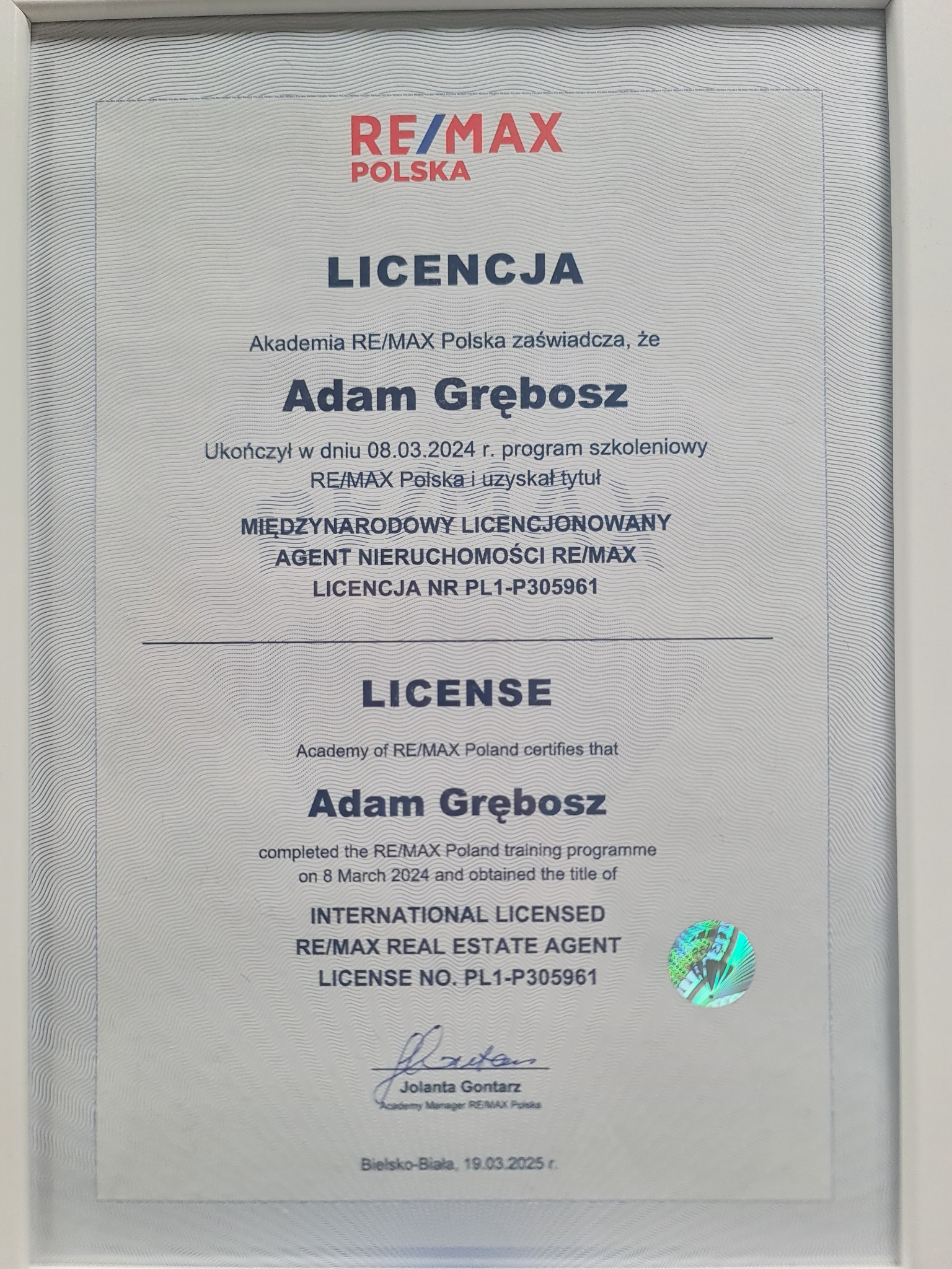 Licencja RE/MAX dla Adama Grębosza, potwierdzająca ukończenie szkolenia i uzyskanie tytułu Międzynarodowego Licencjonowanego Agenta Nieruchomości.