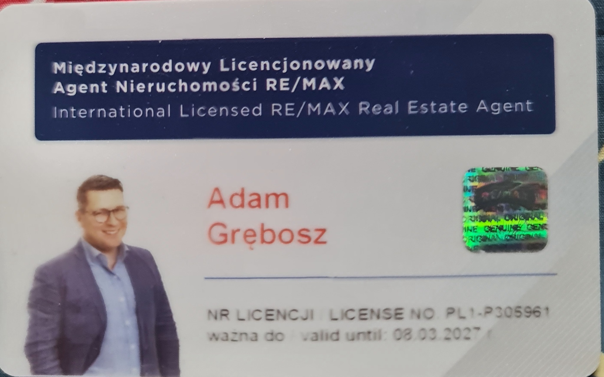 Licencja agenta nieruchomości RE/MAX Adama Grębosza z hologramem, ważna do 08.03.2027. Dokument w formacie karty z danymi osobowymi i zdjęciem.