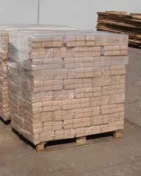 Paleta z brykietem trocinowym dębowym, owinięta folią stretch, widoczna tekstura drewna, w tle stos desek.