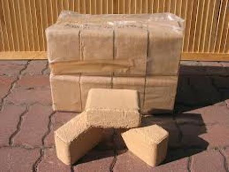 Ułożone na czerwonej kostce brukowej brykiety trocinowe dębowe, zapakowane w folię, z widocznymi fragmentami na pierwszym planie.