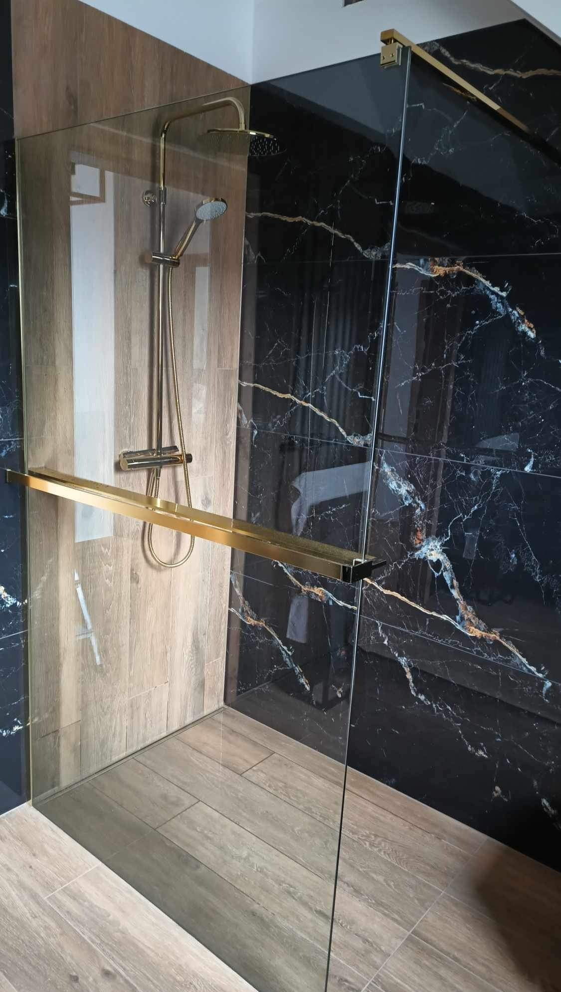 Nowoczesna kabina prysznicowa z czarnymi płytkami imitującymi marmur i drewnopodobnymi płytkami. Złote wykończenia dodają elegancji. Kabina bez brodzika.