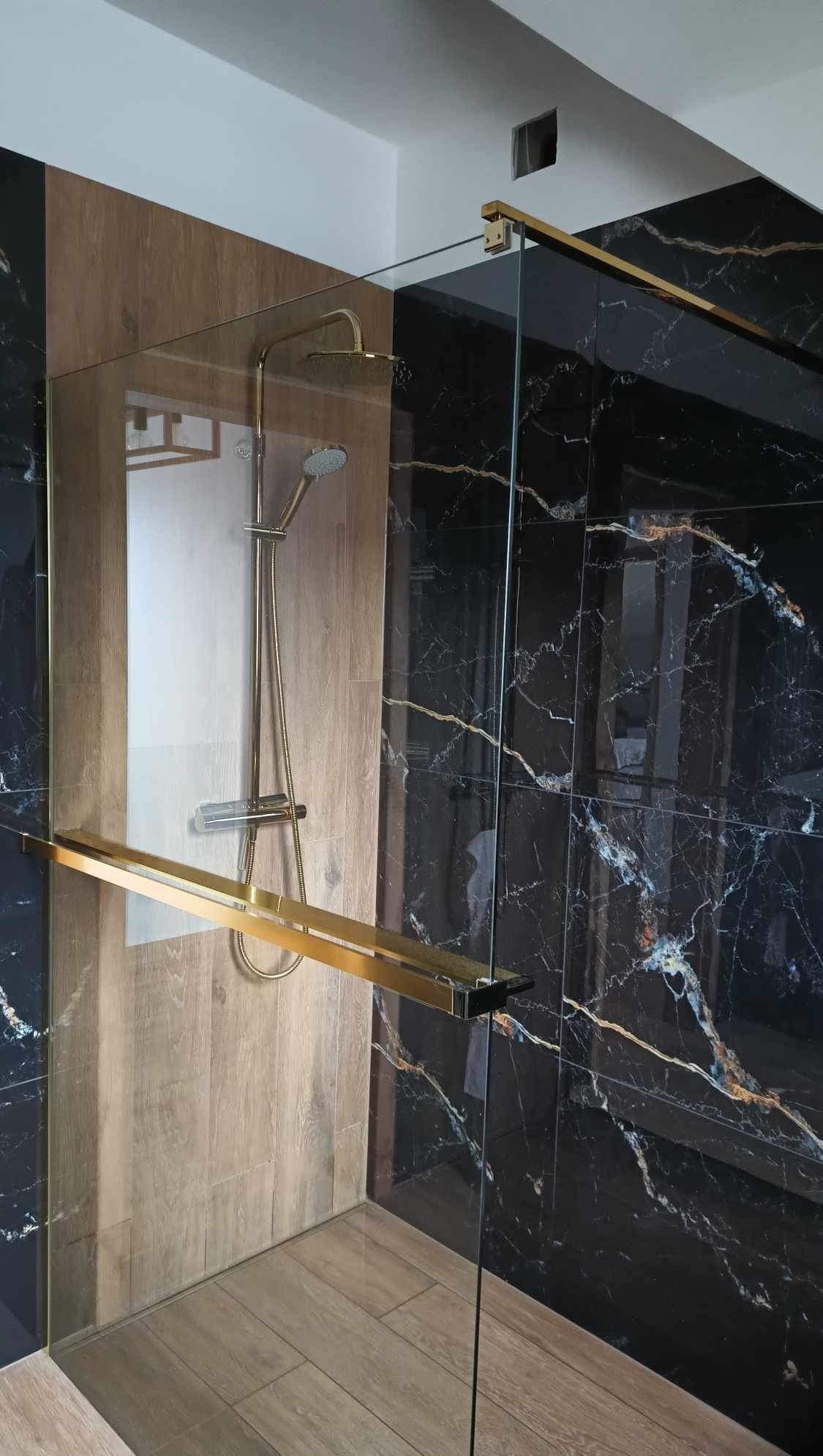 Nowoczesna kabina prysznicowa z czarnymi płytkami imitującymi marmur i drewnopodobnymi panelami. Złote detale armatury i okuć podkreślają elegancki charakter.