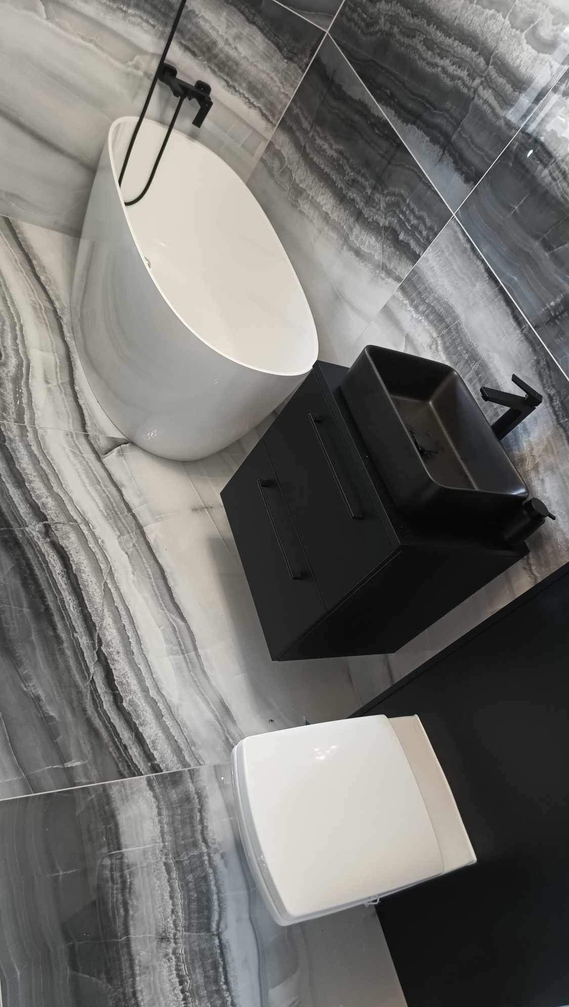 Nowoczesna łazienka w odcieniach szarości i bieli: wolnostojąca wanna, czarna szafka z umywalką i toaleta, marmurowe płytki na podłodze i ścianach.