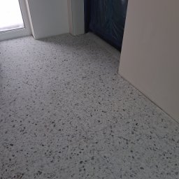 WEST-BUD IHOR MARTSYNKOVSKYI - Szara, wzorzysta posadzka z terazzo w jasnym pomieszczeniu, widok z góry. Fragment okna i drzwi w tle. Minimalistyczny design podłogi.