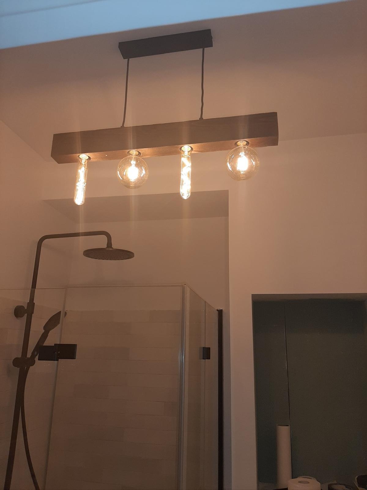 Nowoczesna lampa wisząca z drewnianą belką i czterema żarówkami w łazience z kabiną prysznicową. Ciepłe światło.