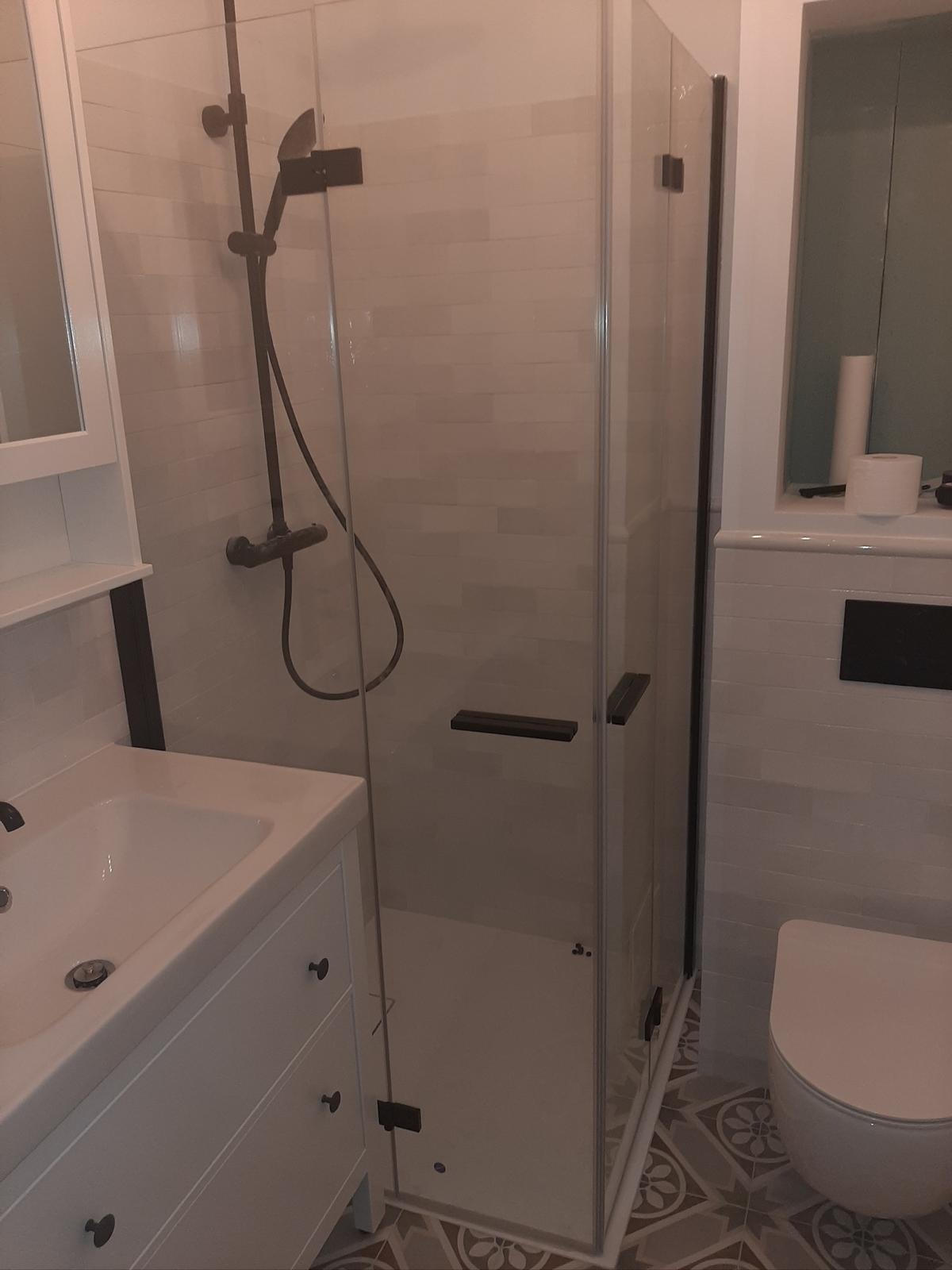 Wykończona łazienka: biała umywalka z szafką, kabina prysznicowa z czarną armaturą i toaleta. Podłoga w geometryczne wzory.