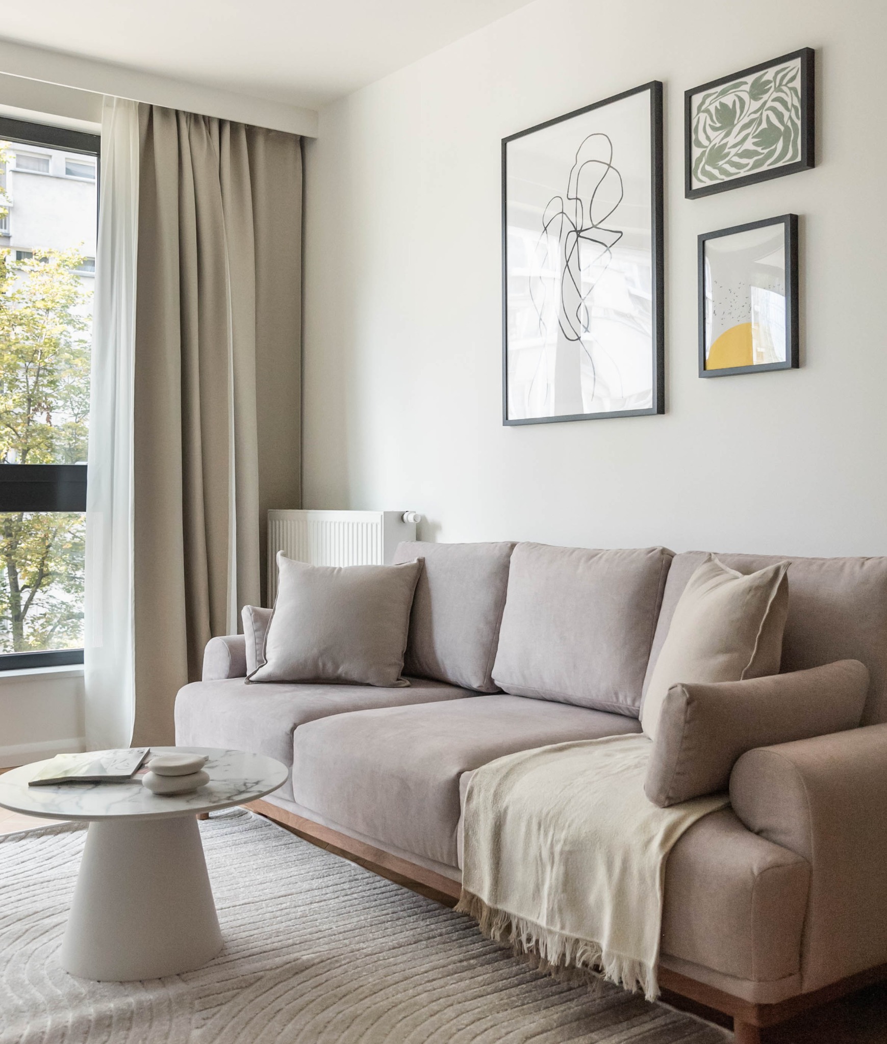 Jasny salon z beżową sofą, okrągłym stolikiem kawowym i dekoracjami ściennymi. Minimalistyczny styl z akcentami naturalnego światła.