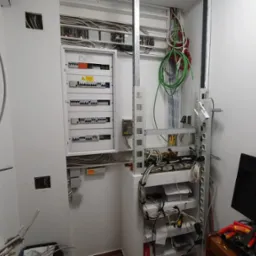 Rozdzielnia elektryczna po montażu w białym pomieszczeniu. Widoczne kable, zabezpieczenia i elementy instalacji. Praca wykonana schludnie i profesjonalnie. 'Po'.