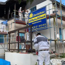 Firmanty Construction & Design - Ekipa w kombinezonach na rusztowaniu, ocieplająca elewację domu jednorodzinnego. Widoczny baner reklamowy firmy budowlanej i narzędzia pracy.