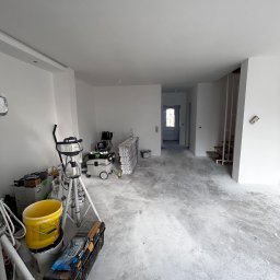 MydMar - Wnętrze w trakcie prac wykończeniowych: świeżo pomalowane, białe ściany, narzędzia malarskie, szpachle i drabina w pomieszczeniu. Widoczne przygotowania do dalszych prac.