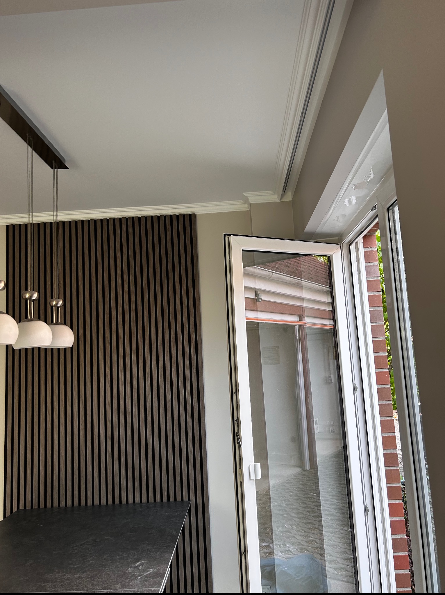 Nowoczesne wnętrze z drewnianą ścianą panelową, wiszącą lampą i otwartym oknem balkonowym z widokiem na zewnątrz. Minimalistyczny design i neutralna kolorystyka.