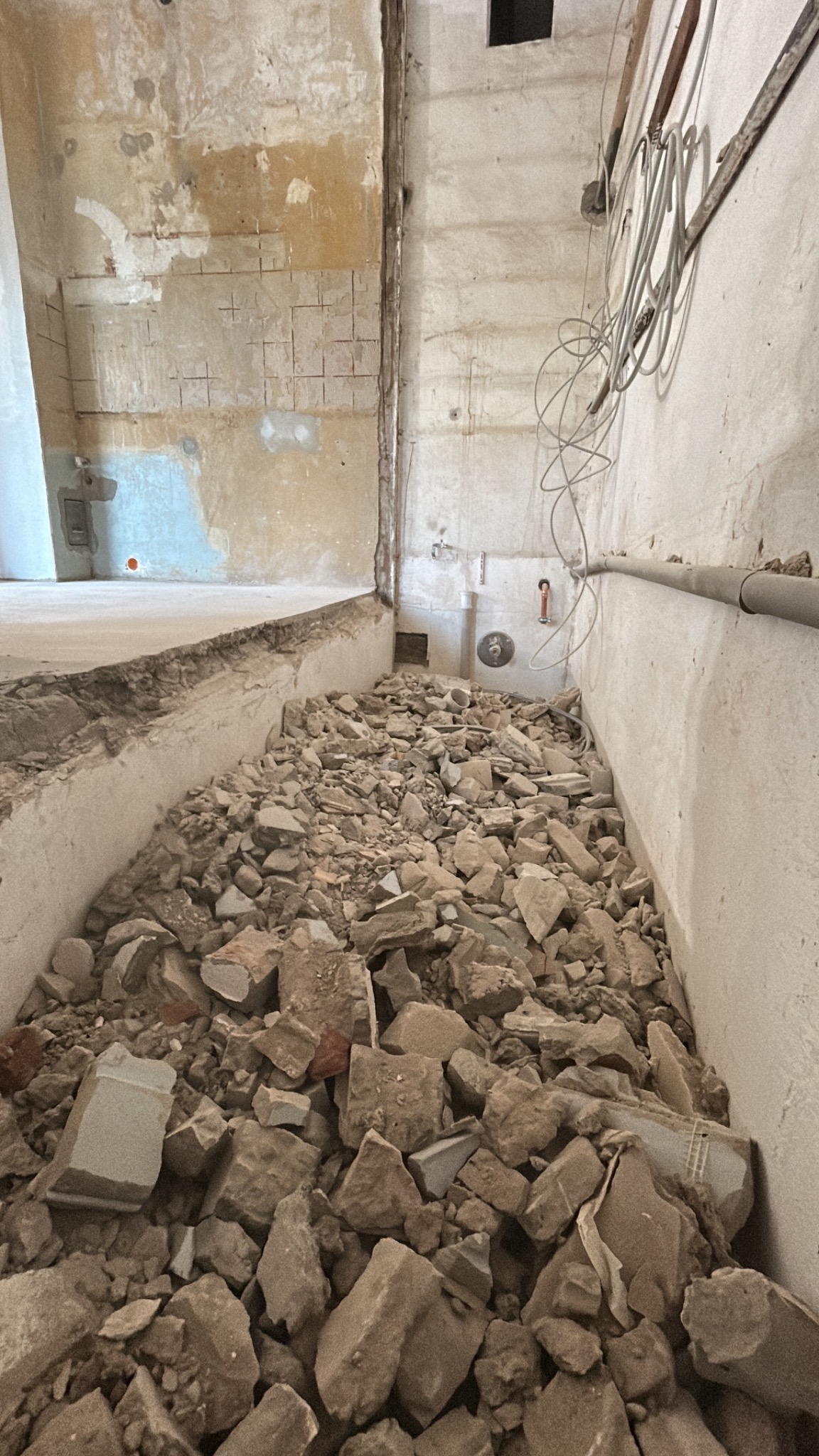 Wnętrze w trakcie demontażu. Gruz na podłodze, ściany z widocznymi śladami po instalacjach. Kable zwisają ze ściany. Etap przygotowawczy do remontu.