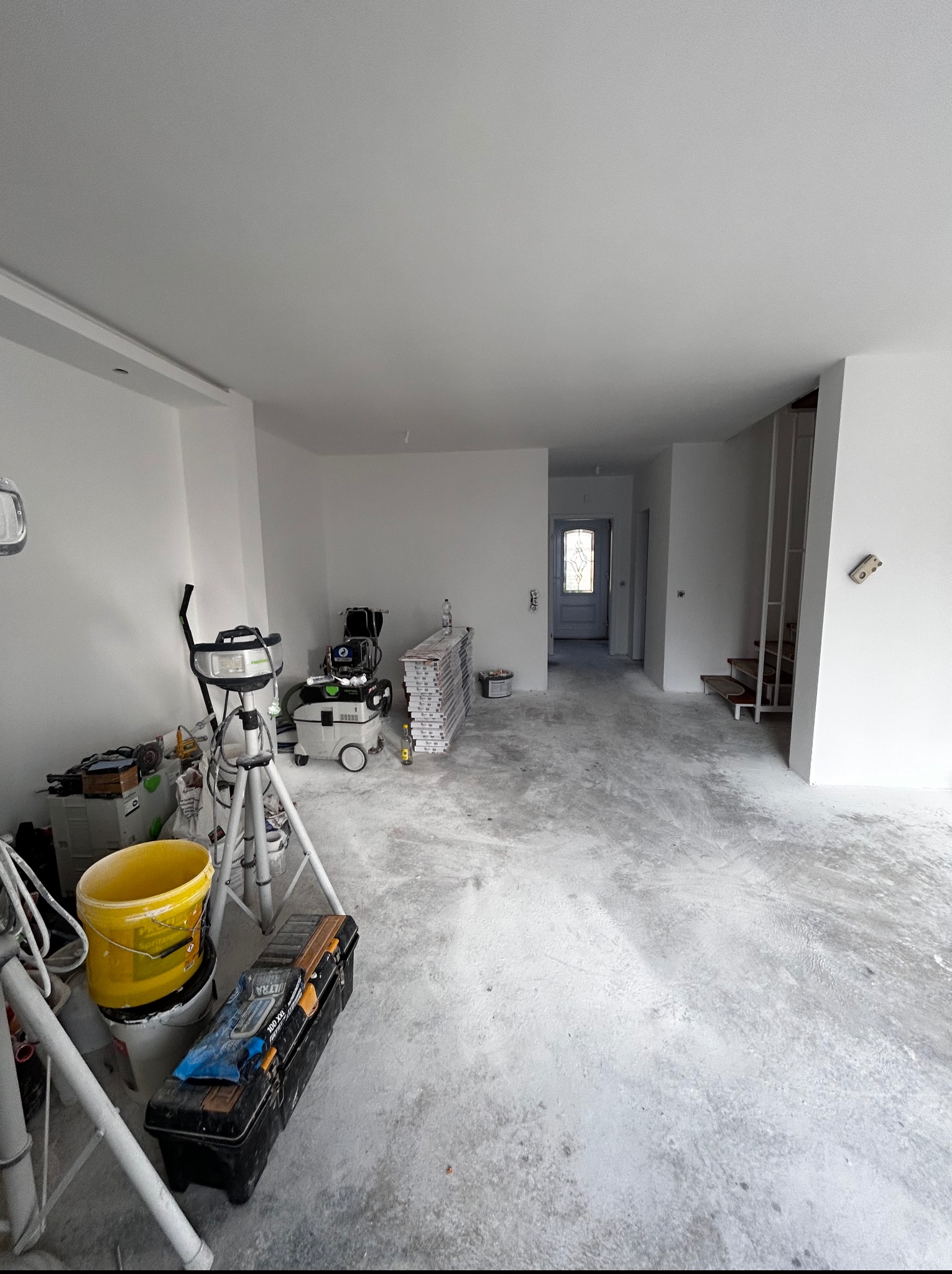 Wnętrze w trakcie prac wykończeniowych: świeżo pomalowane, białe ściany, narzędzia malarskie, szpachle i drabina w pomieszczeniu. Widoczne przygotowania do dalszych prac.