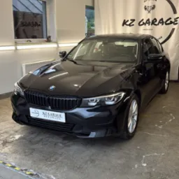 Błyszczący, czarny BMW serii 3 po detailingu w garażu KZ Garage, widoczne logo firmy na tle. Auto prezentuje się czysto i elegancko.