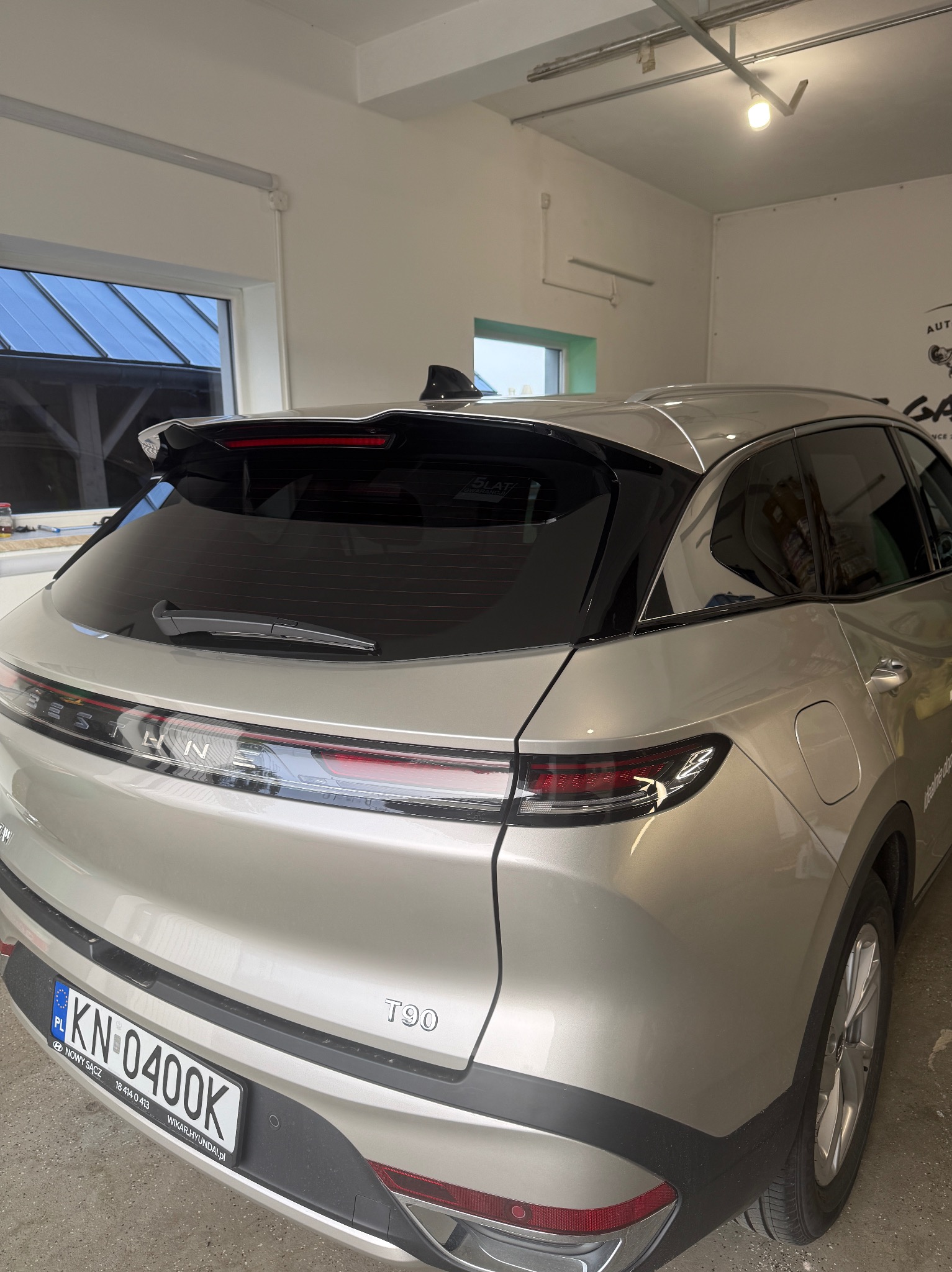 Przyciemnione szyby w srebrnym samochodzie Bestune T90, widoczne tylne okno i szyby boczne. Detal: polska tablica rejestracyjna.