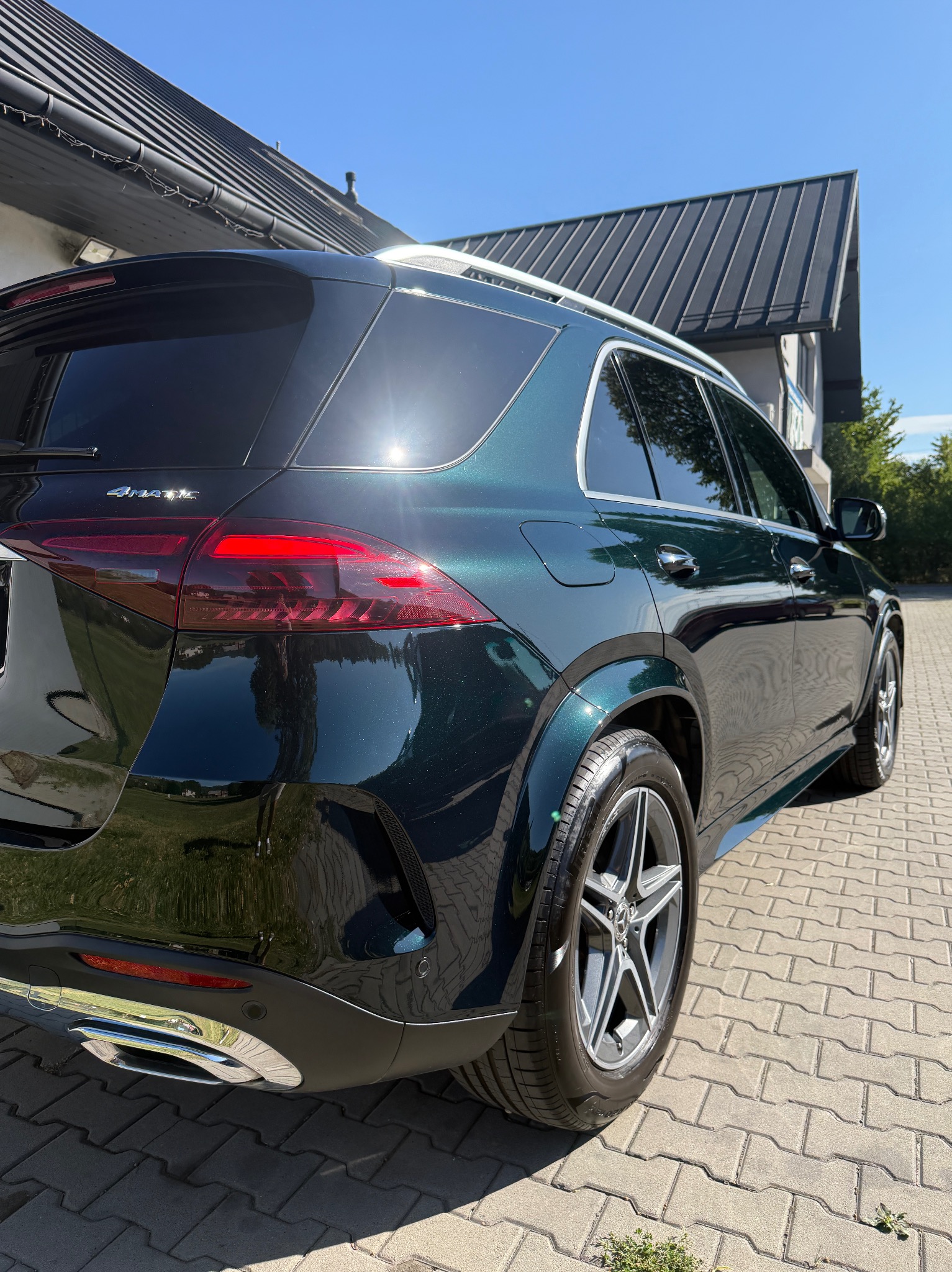 Błyszczący, ciemnozielony Mercedes GLE po detailingu, widoczny z tyłu na kostce brukowej w słoneczny dzień. Chromowane elementy i czyste opony.
