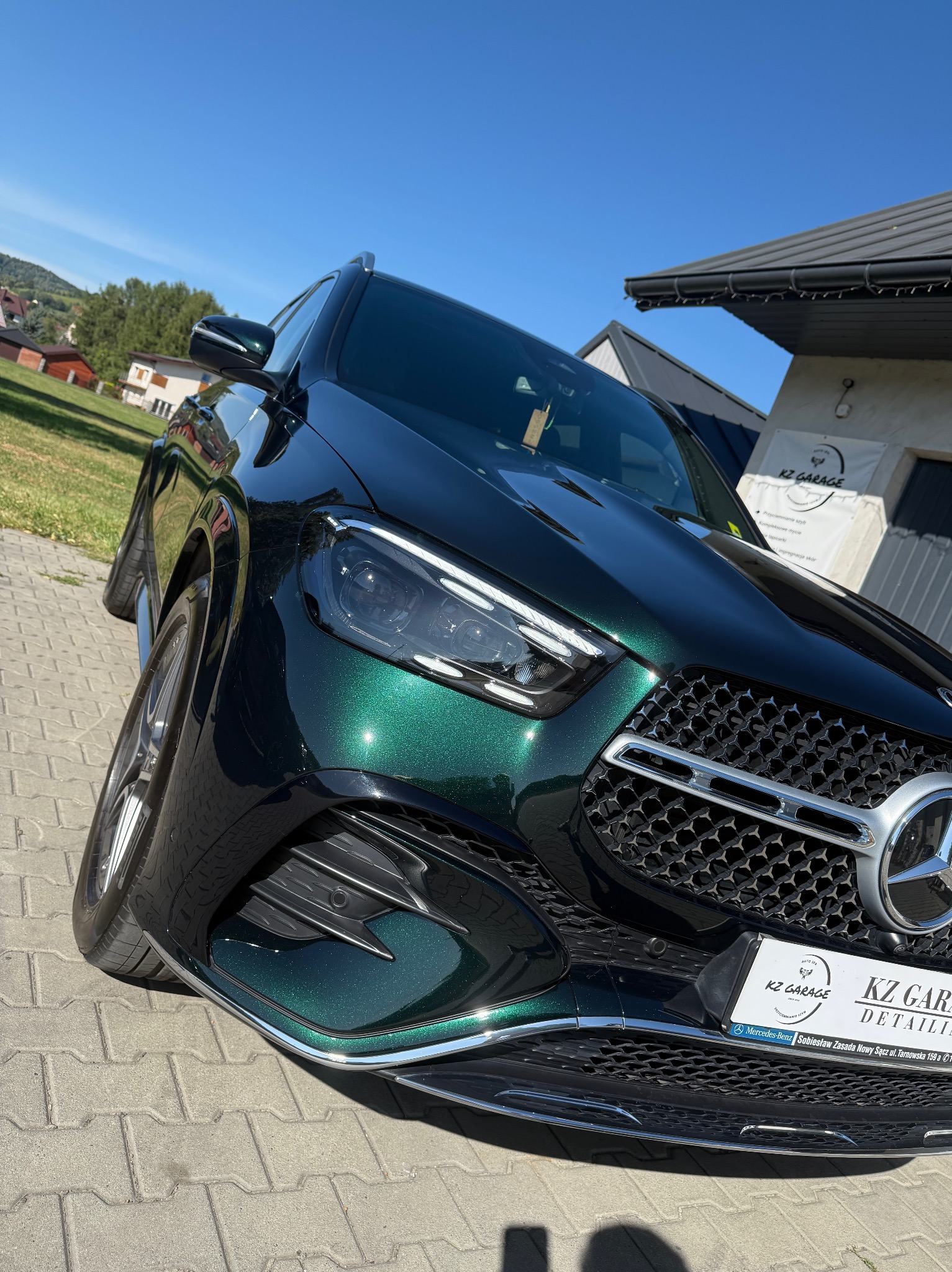 Mercedes GLC w głębokiej, zielonej barwie, po detailingu w KZ Garage. Widoczny grill, reflektor, logo i fragment budynku firmy. Słoneczny dzień.