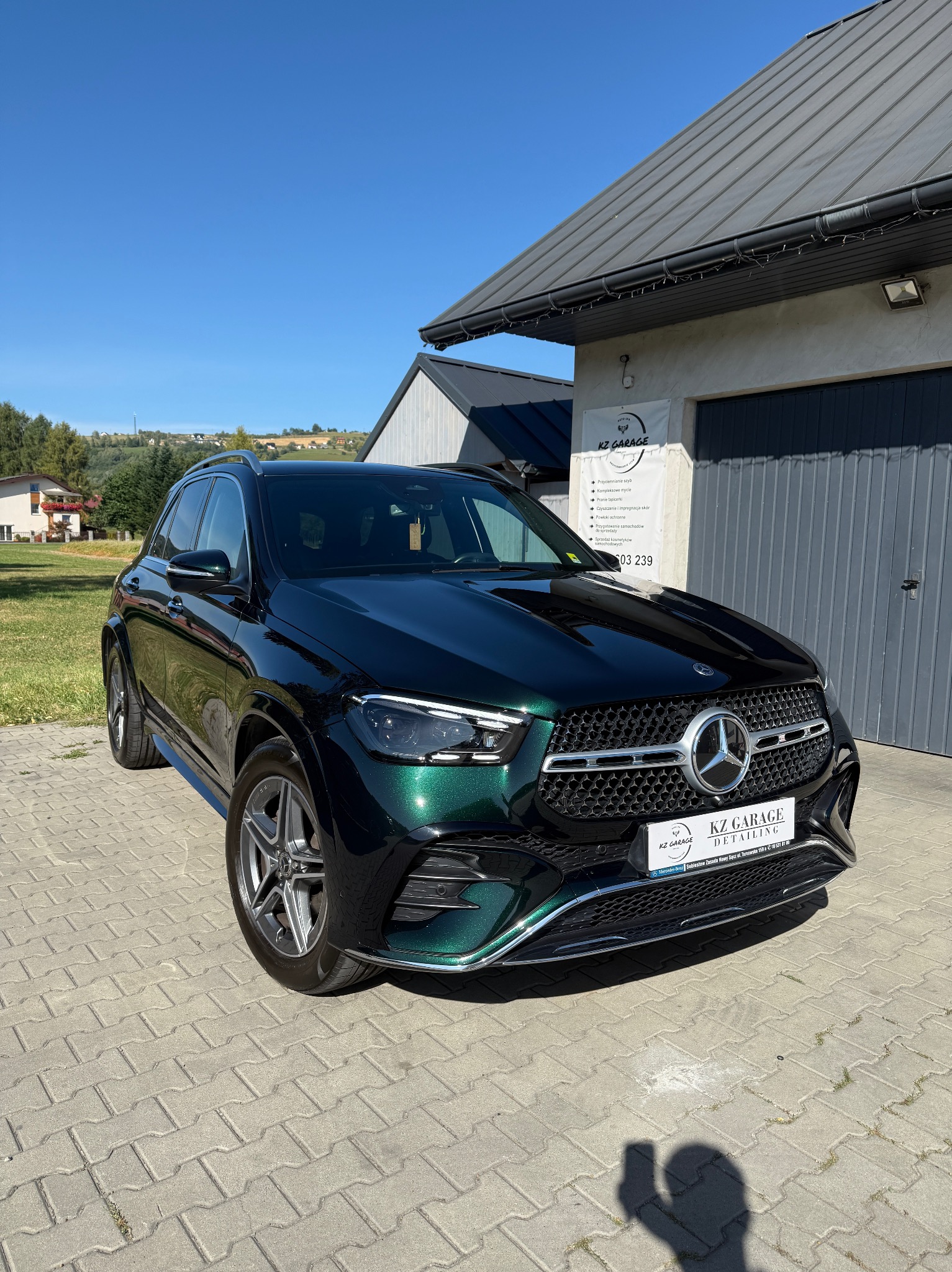 Błyszczący, zielony Mercedes GLE po detailingu, zaparkowany przed garażem z logo KZ Garage, w słoneczny dzień. Widoczne odbicia w lakierze.