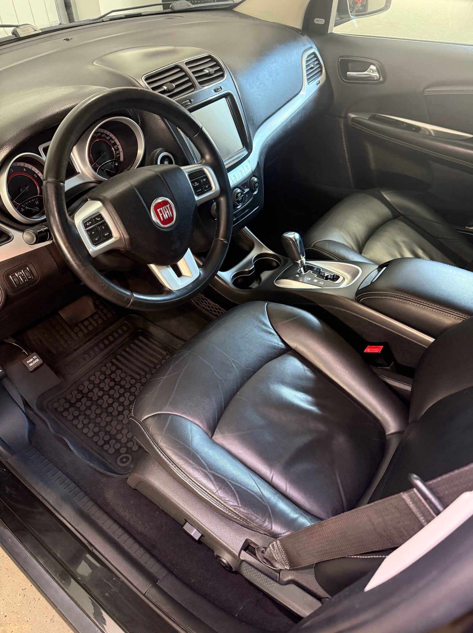 Wnętrze samochodu marki Fiat z czarną skórzaną tapicerką, widok na deskę rozdzielczą, kierownicę z logo, fotele i konsolę środkową.