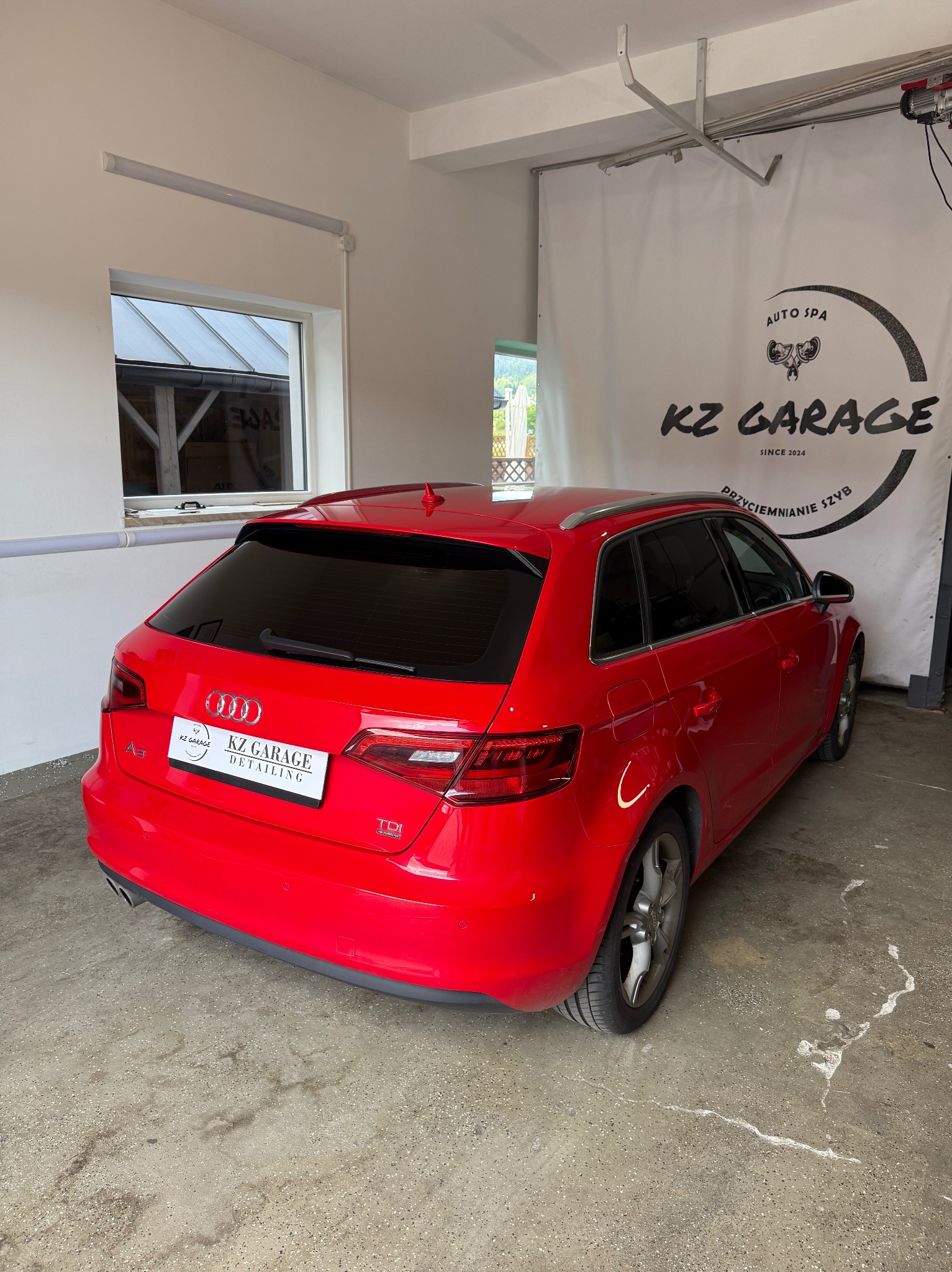 Czerwone Audi A3 po usłudze auto detailingu z przyciemnionymi szybami, zaparkowane w garażu z logo KZ Garage. Widoczny błyszczący lakier i czyste felgi.
