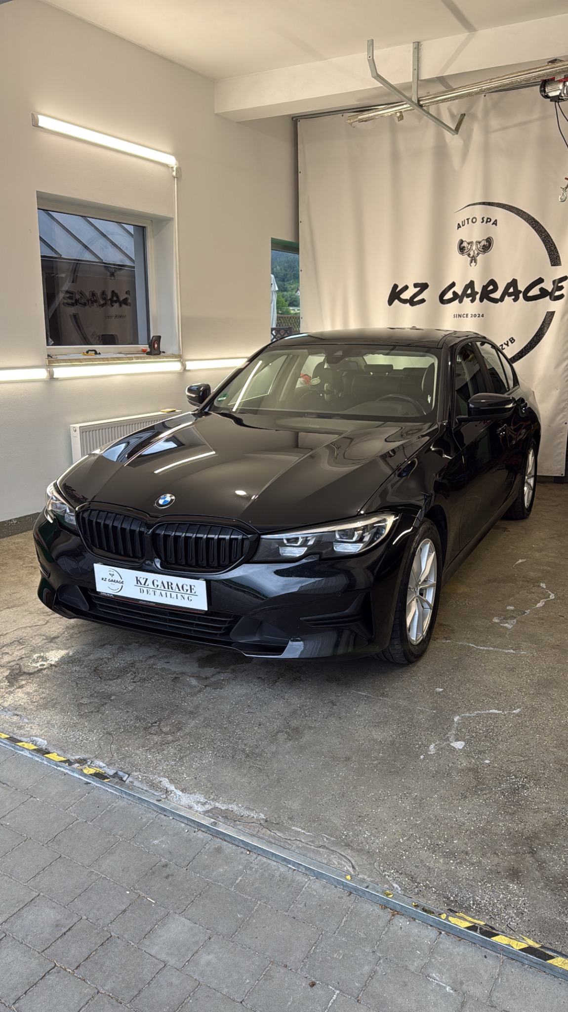 Błyszczący, czarny BMW serii 3 po detailingu w garażu KZ Garage, widoczne logo firmy na tle. Auto prezentuje się czysto i elegancko.