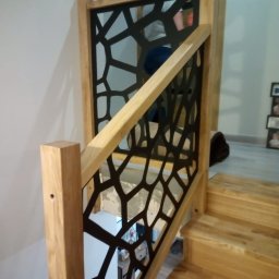 Qest meble - Drewniane schody z nowoczesną balustradą o geometrycznym wzorze. Jasne drewno i czarne elementy tworzą kontrast. Widok z góry na stopnie.