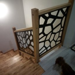 Qest meble - Drewniane schody z ozdobną balustradą o geometrycznym wzorze, widok z góry. Jasne drewno i czarne wypełnienie tworzą nowoczesny design.