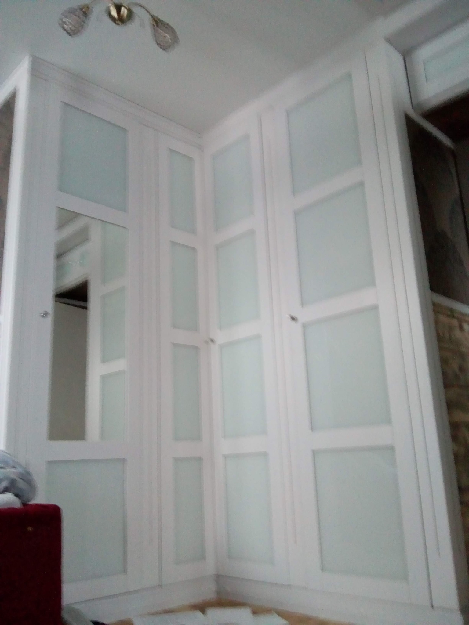 Biała szafa wnękowa z matowymi szybami i lustrem, ujęcie z dołu, widoczna lampa sufitowa.