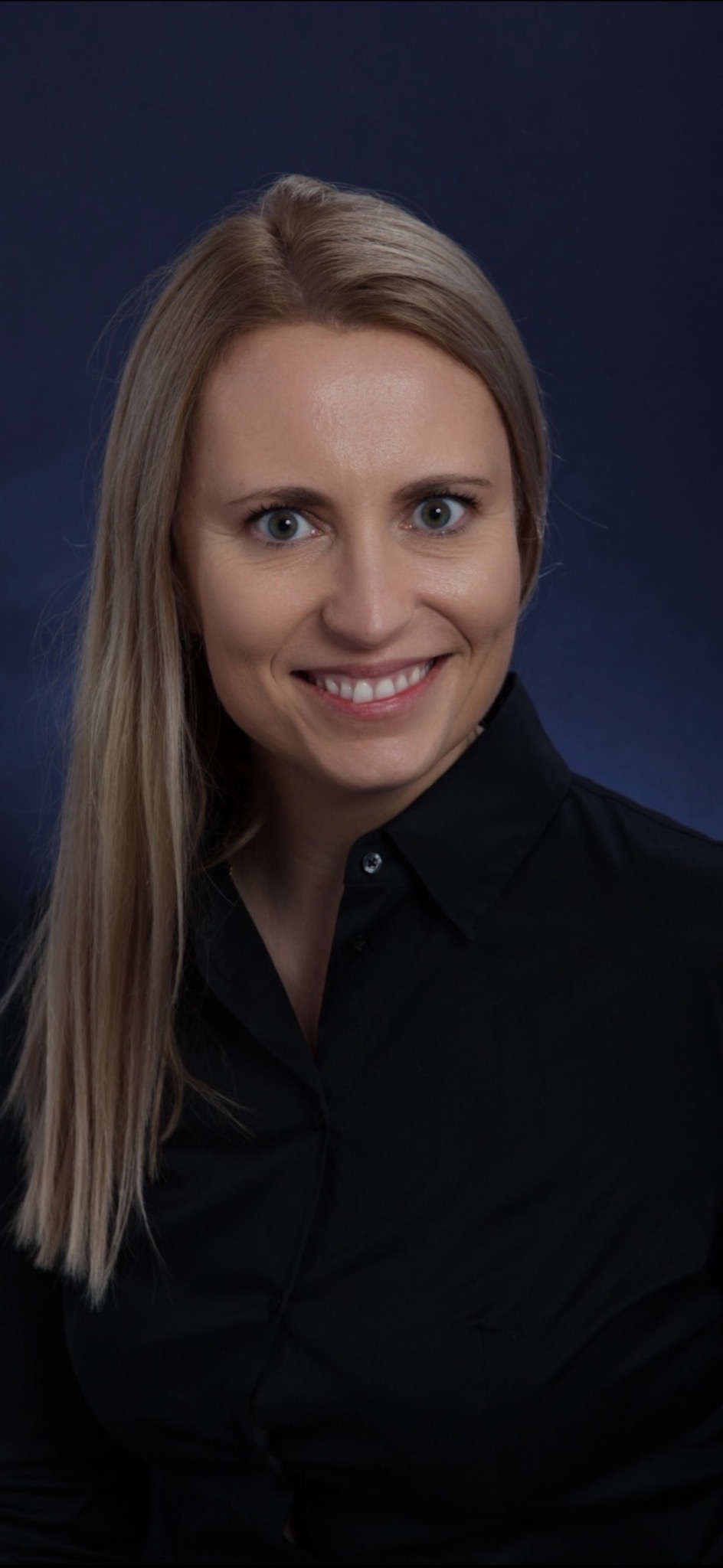 Portret uśmiechniętej blondynki w czarnej koszuli na ciemnoniebieskim tle. Widoczne zielone oczy i śnieżnobiały uśmiech. Profesjonalny wizerunek.