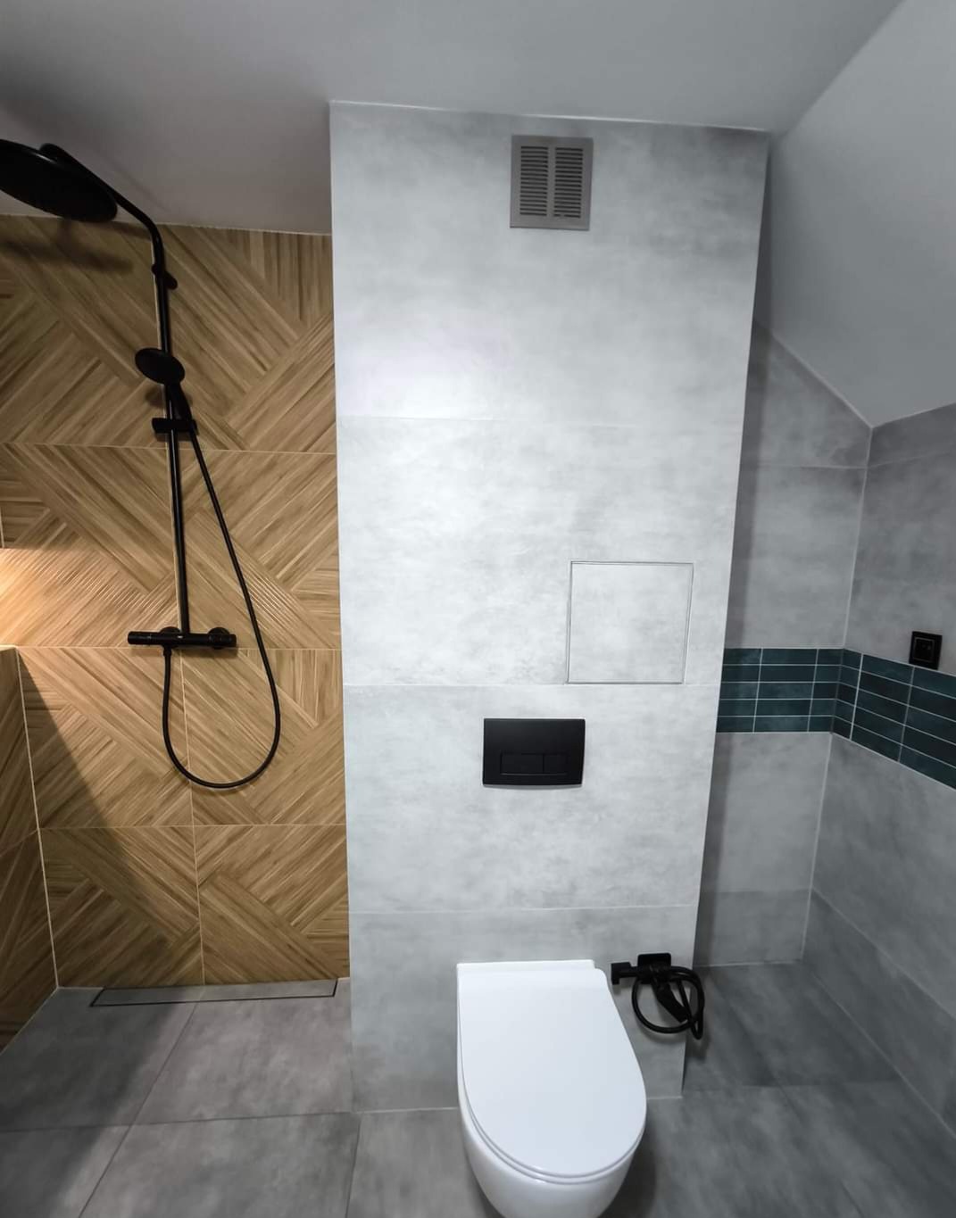 Nowoczesna łazienka z kabiną prysznicową, wykończona płytkami w odcieniach szarości i beżu, z czarną armaturą i podtynkową spłuczką.