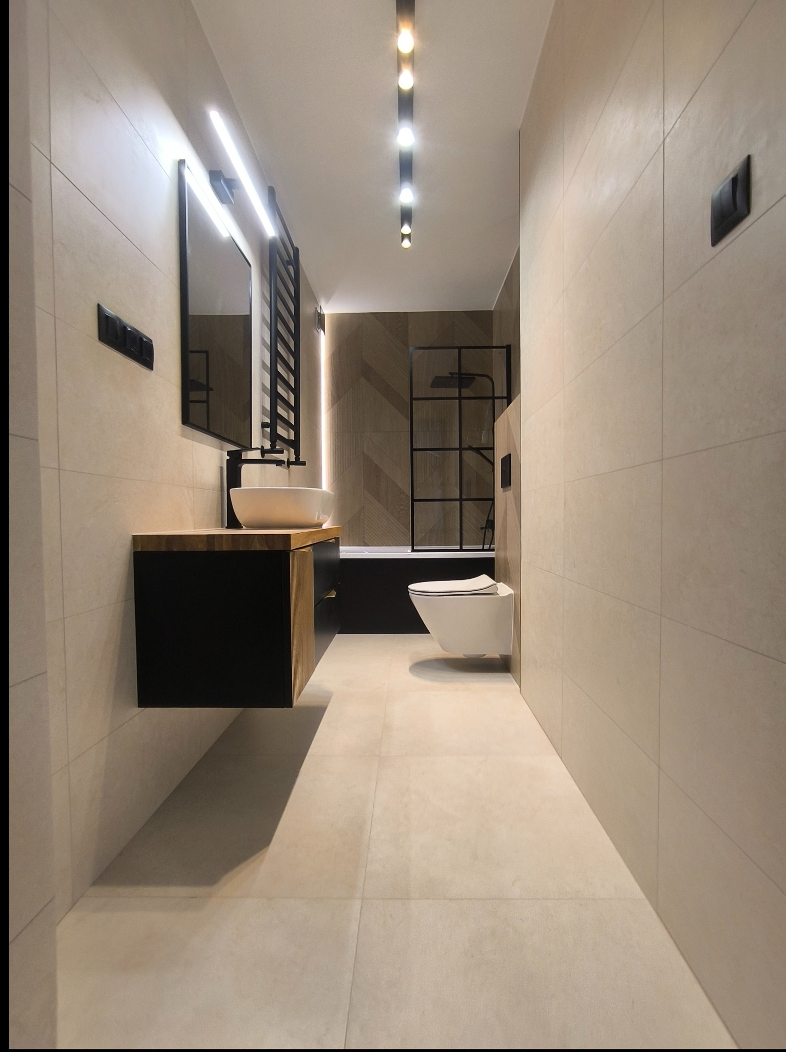 Nowoczesna łazienka z beżowymi płytkami, czarną armaturą i podświetlanym lustrem. Umywalka nablatowa na szafce z drewnianym blatem.