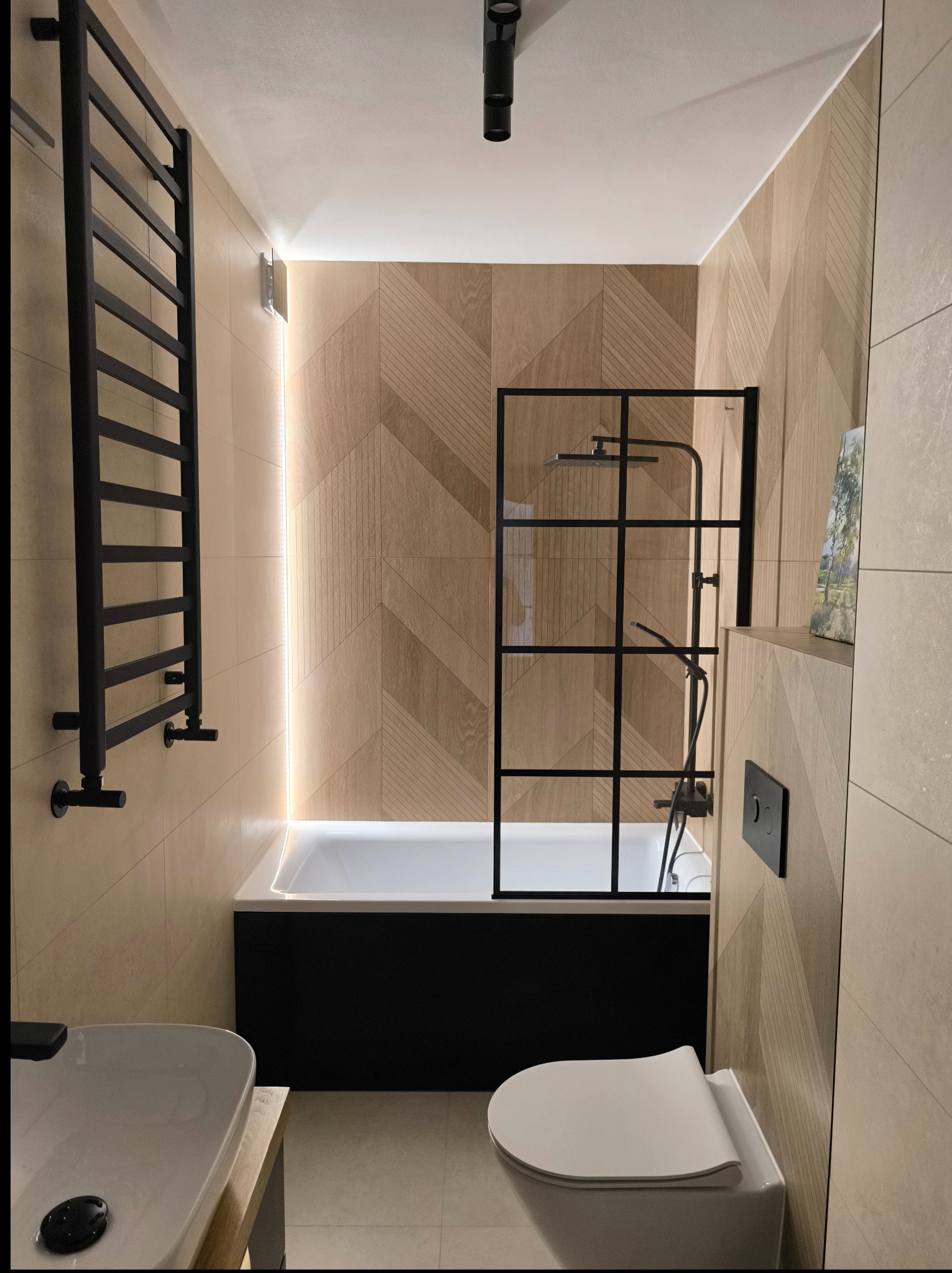 Nowoczesna łazienka z drewnopodobnymi płytkami ułożonymi w geometryczny wzór, czarną armaturą i podświetleniem LED. Minimalistyczny design, ciepłe barwy.