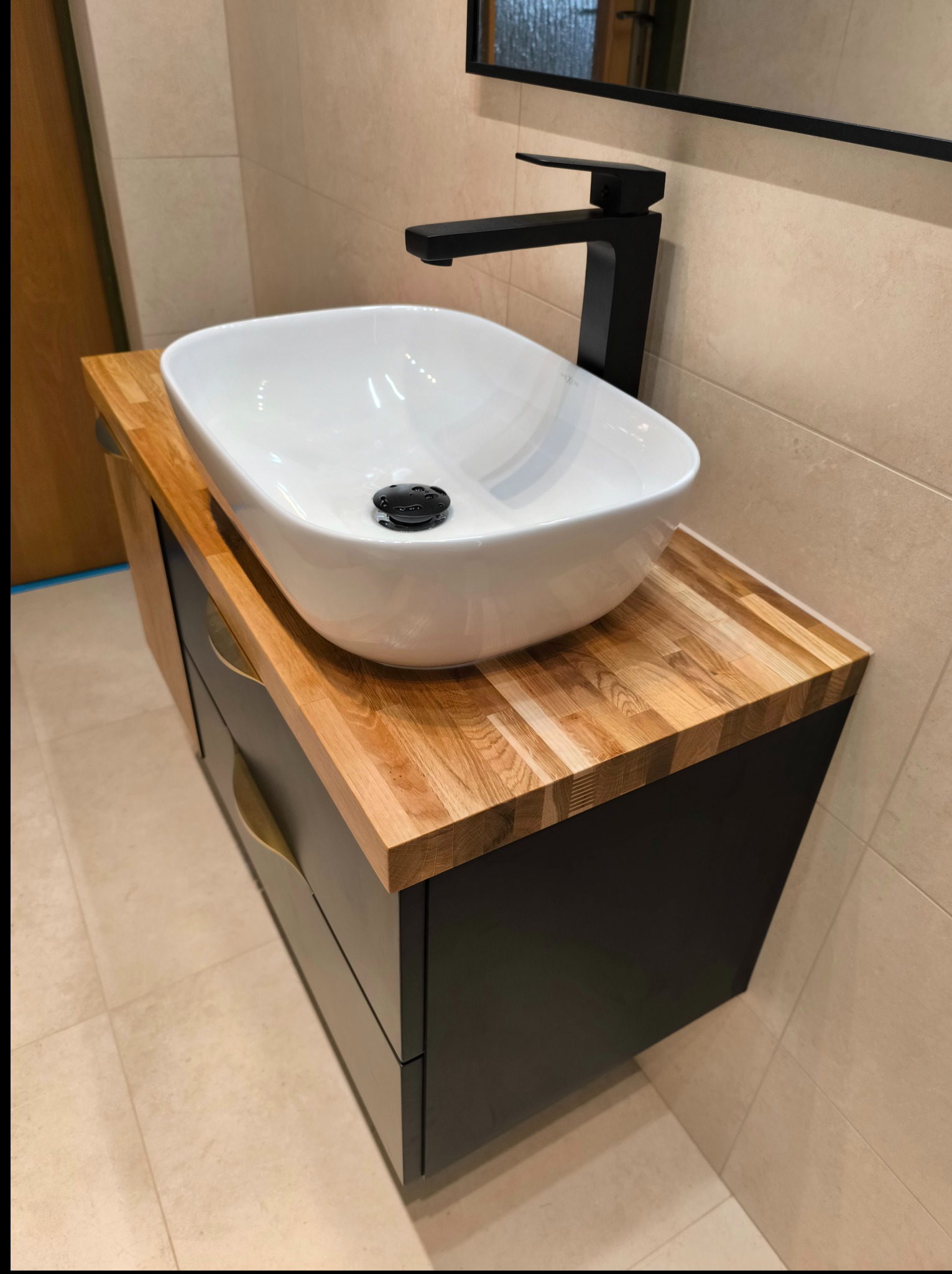 Nowoczesna łazienka: biała umywalka nablatowa na szafce z drewnianym blatem i czarną armaturą. Beżowe płytki na ścianach i podłodze.