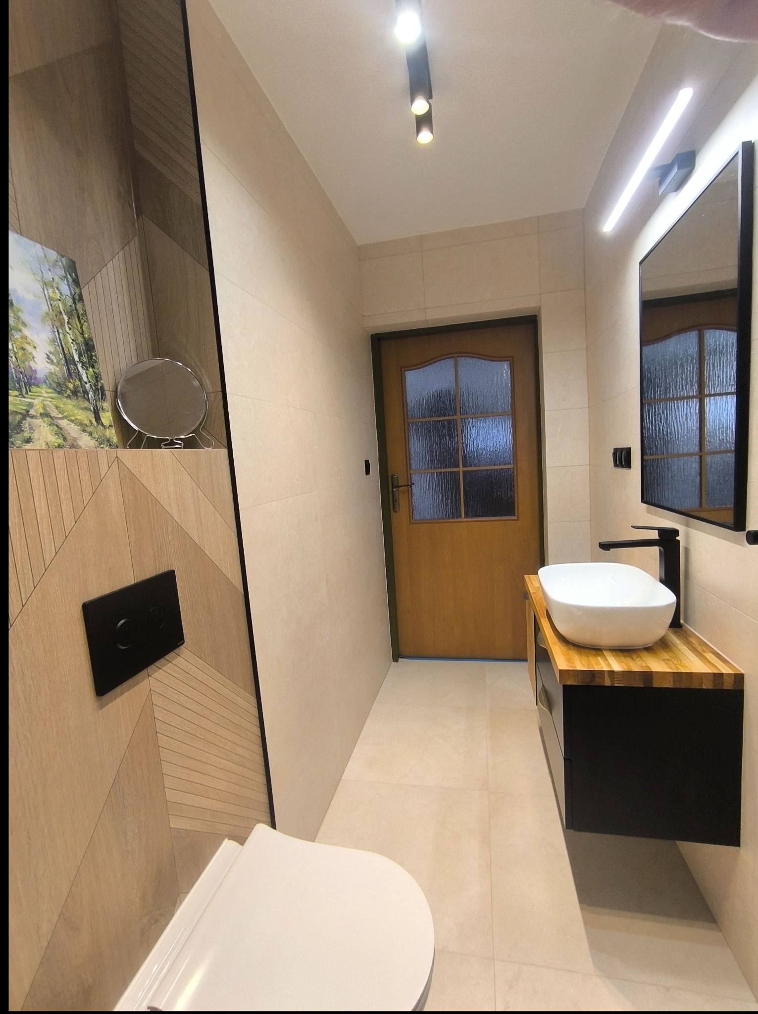 Nowoczesna aranżacja łazienki w Błoniu: drewniane akcenty na ścianach i blacie pod umywalką, minimalistyczna armatura i oświetlenie punktowe. Elegancki design.