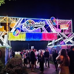 Agencja Reklamowa ActionPrint - Iluminowana brama wejściowa na Kortowiadę z logo sponsorów (T-Mobile, Perła) i hasłem 'Future is here'. Tłum ludzi w tle, noc, oświetlenie neonowe.