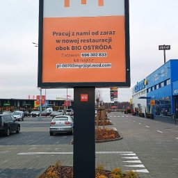 Agencja Reklamowa ActionPrint - Billboard McDonald's przy parkingu centrum handlowego BIG Ostróda, zachęcający do pracy w nowej restauracji. Widoczne logo i dane kontaktowe w kolorze pomarańczowym.