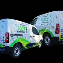 Dwa białe samochody dostawcze z ekologicznymi grafikami i hasłami 'Jestem w 100% elektryczny' oraz 'Pomagajmy Ziemi codziennie'. Widoczne numery rejestracyjne.