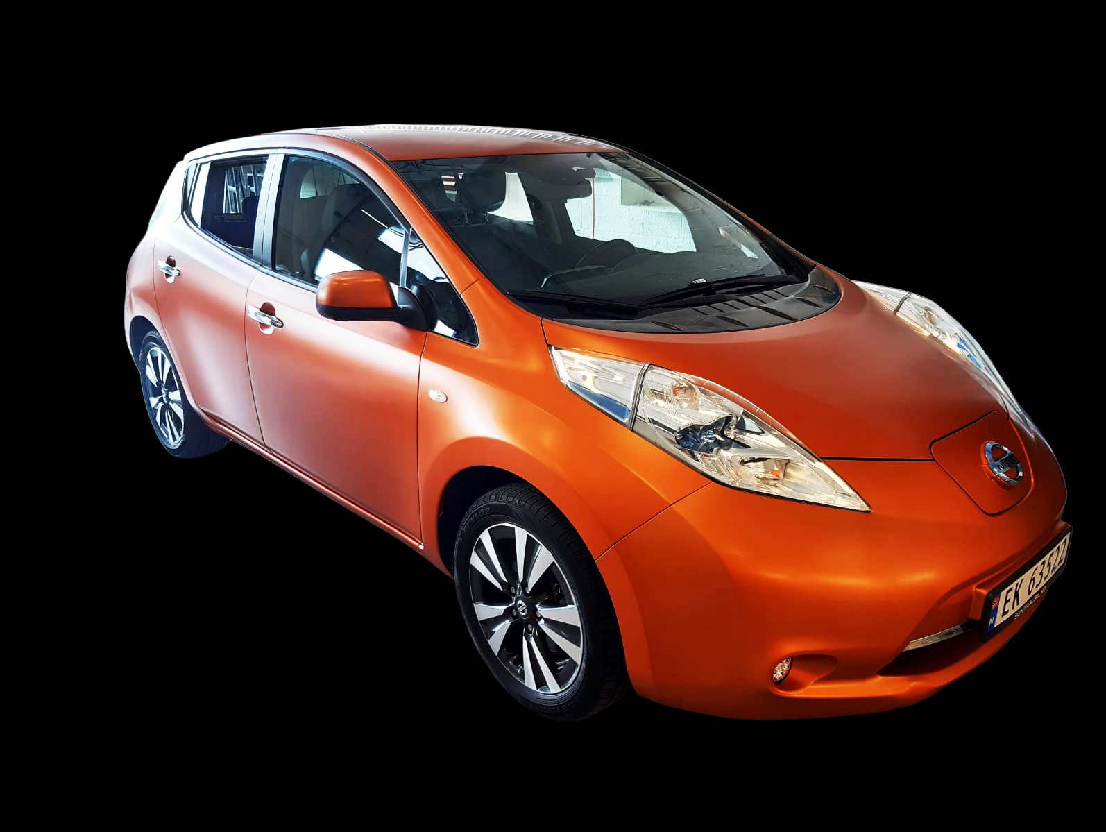 Pomarańczowy, matowy Nissan Leaf na czarnym tle. Ujęcie z boku, widoczne przednie światła i felgi. Auto po detailingu, zmiana koloru folią.