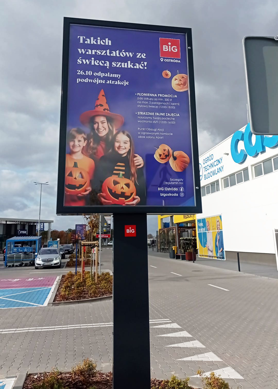 Billboard reklamowy 'BIG Ostróda' z motywem Halloween: warsztaty wycinania dyń i promocje. Dzieci z dyniami, kobieta w kapeluszu czarownicy.