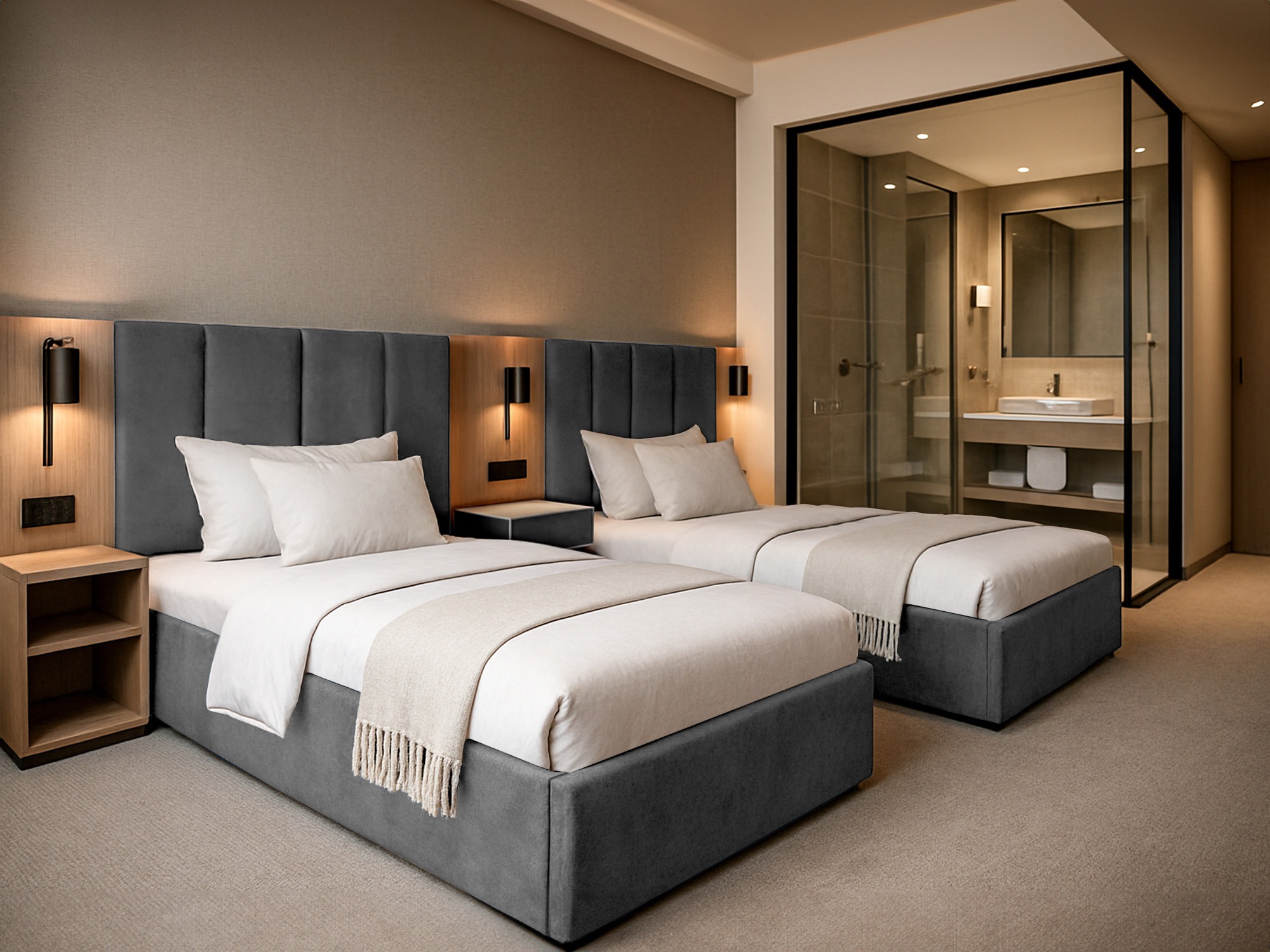 Dwie szare, tapicerowane sofy z zagłówkami w pokoju hotelowym, z widoczną łazienką za szklaną ścianą. Minimalistyczny design, ciepłe oświetlenie.