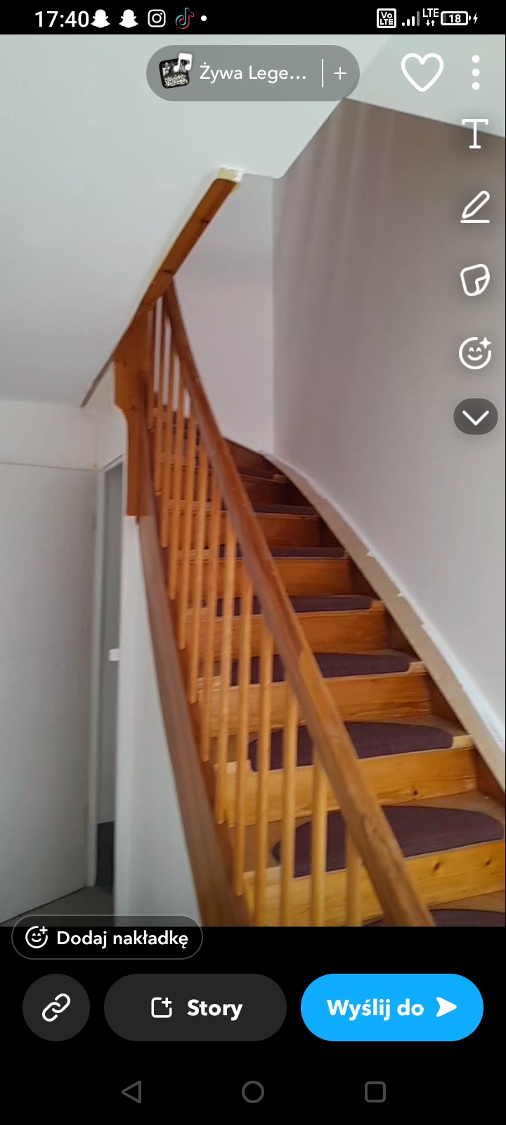 Drewniane schody z brązowymi nakładkami na stopniach, prowadzące w górę w jasnym wnętrzu. Widoczne białe ściany i fragment drzwi.