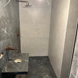 Daydrems Damian Hula - Nowoczesna łazienka w trakcie wykańczania: marmurowe płytki, złota armatura, zamontowana umywalka. Widoczne przewody i taboret.